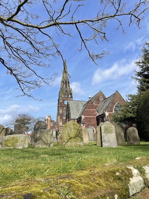 Church in the back ground and gravestones in the foreground on a blue sky day
